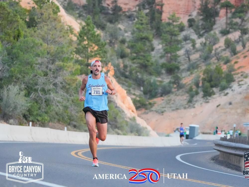 Alex T. Baker on the Bryce Canyon Half course, running a curved mountain road lined with pines and red rock, same singlet and bib 78101.